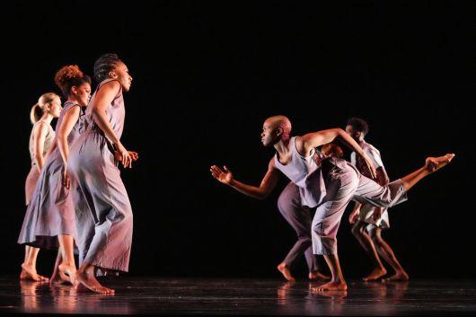 People in flowy grey gowns in contempary dance positions against a black backdrop.